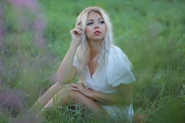  На фото героиня текста Татьяна Лугвина позирует в высокой траве, сидя в белом коротком платье.