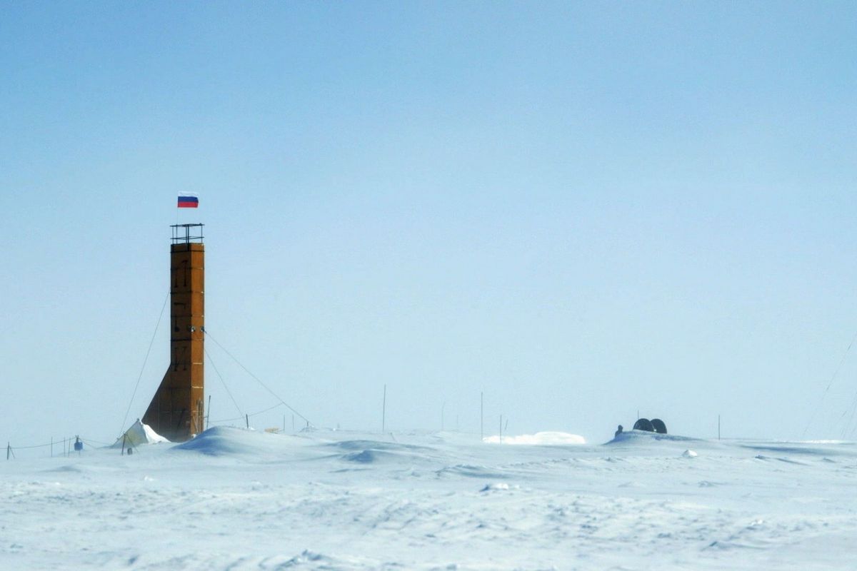  На фотографии заснеженный пейзаж с кирпичной башней, над которой зазвивается российский триолор.
