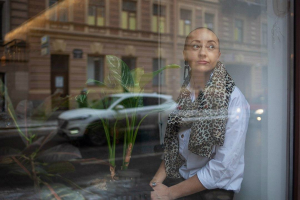  На фотографии, снятой сквозь витрину уличного кафе, яркая женщина с очень короткой стрижкой.